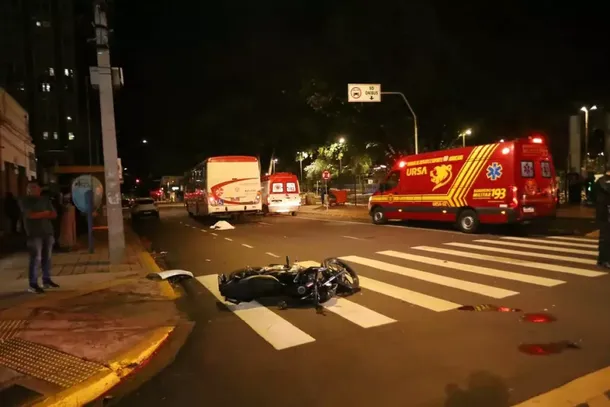 Motocicleta Honda Fan 160 ca&iacute;da na esquina da Pra&ccedil;a Ary Coelho, regi&atilde;o central de Campo Grande; corpo da v&iacute;tima aparece ao fundo, coberto por len&ccedil;ol branco. (Foto: Paulo Francis)