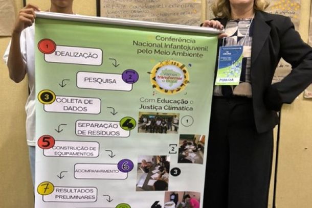Aluno Miguel e a pedagoga M&aacute;rcia Langner apresentam banner levado &agrave; Confer&ecirc;ncia Nacional Infantojuvenil pelo Meio Ambiente (CNIJMA), em 2025, onde o projeto conquistou primeiro lugar com nota m&aacute;xima